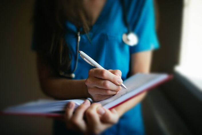 Woman in teal nursing scrubs and stethoscope writing notes in a notebook